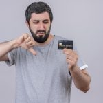 Uomo insoddisfatto guarda una carta di credito e mostra il pollice verso, simbolo di disapprovazione, rappresentando le frustrazioni comuni legate alle carte di credito in Italia.