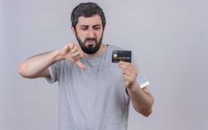 Uomo insoddisfatto guarda una carta di credito e mostra il pollice verso, simbolo di disapprovazione, rappresentando le frustrazioni comuni legate alle carte di credito in Italia.