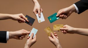 Un gruppo di mani che tengono diverse carte bancarie colorate su sfondo neutro, rappresentando le varie opzioni di pagamento disponibili: carte di debito, credito e revolving.