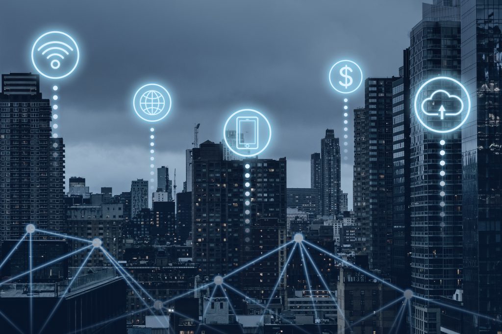 Veduta urbana di una grande città al tramonto con grattacieli moderni, sovrapposta a icone digitali luminose che rappresentano connessioni Wi-Fi, rete globale, smartphone, denaro e cloud. Le linee connesse tra gli edifici illustrano un'infrastruttura tecnologica avanzata, simbolo dello sviluppo digitale urbano. L'immagine evoca l'ecosistema dell'innovazione e della digitalizzazione finanziaria, contesto in cui la Fintech in Italia sta emergendo con soluzioni smart per la gestione economica e bancaria attraverso piattaforme integrate e connesse.