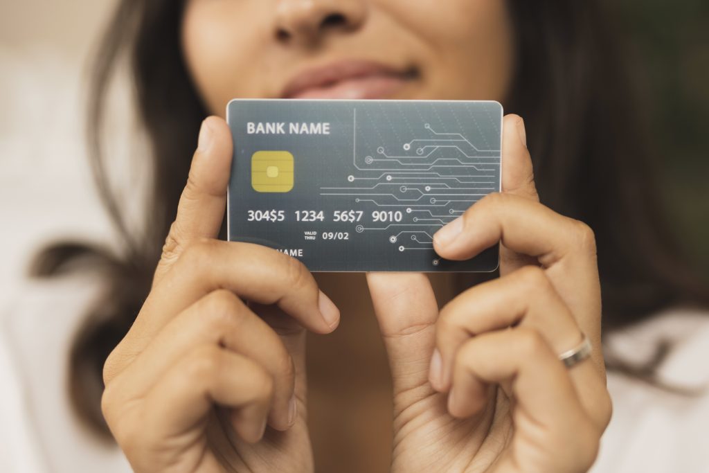 Una donna tiene in mano una carta di credito con design futuristico, chip dorato e circuito stampato visibile sul lato destro. Il nome della banca è generico e i numeri della carta sono parzialmente fittizi. L'immagine rappresenta l'evoluzione digitale dei pagamenti e il ruolo crescente delle carte di credito co-branded nel semplificare l'esperienza finanziaria personalizzata.