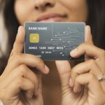Una donna tiene in mano una carta di credito con design futuristico, chip dorato e circuito stampato visibile sul lato destro. Il nome della banca è generico e i numeri della carta sono parzialmente fittizi. L'immagine rappresenta l'evoluzione digitale dei pagamenti e il ruolo crescente delle carte di credito co-branded nel semplificare l'esperienza finanziaria personalizzata.