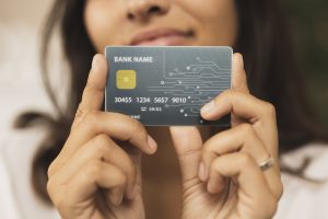 Una donna tiene in mano una carta di credito con design futuristico, chip dorato e circuito stampato visibile sul lato destro. Il nome della banca è generico e i numeri della carta sono parzialmente fittizi. L'immagine rappresenta l'evoluzione digitale dei pagamenti e il ruolo crescente delle carte di credito co-branded nel semplificare l'esperienza finanziaria personalizzata.