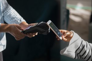Una persona effettua un pagamento contactless avvicinando il proprio smartphone a un terminale POS tenuto da un'altra persona. Sullo schermo del telefono si vede chiaramente l'applicazione di pagamento che indica l'autorizzazione alla transazione. L'immagine rappresenta l'uso di tecnologie moderne per i pagamenti istantanei, evidenziando la comodità e la rapidità delle soluzioni digitali nella vita quotidiana.