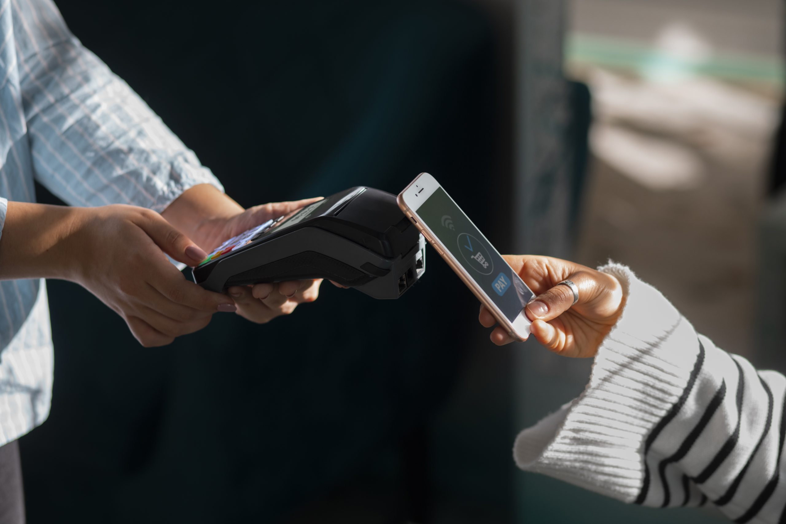 Una persona effettua un pagamento contactless avvicinando il proprio smartphone a un terminale POS tenuto da un'altra persona. Sullo schermo del telefono si vede chiaramente l'applicazione di pagamento che indica l'autorizzazione alla transazione. L'immagine rappresenta l'uso di tecnologie moderne per i pagamenti istantanei, evidenziando la comodità e la rapidità delle soluzioni digitali nella vita quotidiana.