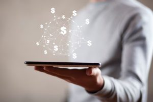 Concetto digitale di Fintech con simboli di dollaro fluttuanti sopra un tablet tenuto da una persona, rappresentando l’innovazione tecnologica nei servizi finanziari.