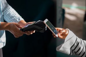 Una persona effettua un pagamento contactless con uno smartphone utilizzando carte di credito digitali, avvicinando il dispositivo a un terminale POS tenuto da un'altra persona. L'immagine rappresenta un ambiente moderno e tecnologico per i pagamenti.