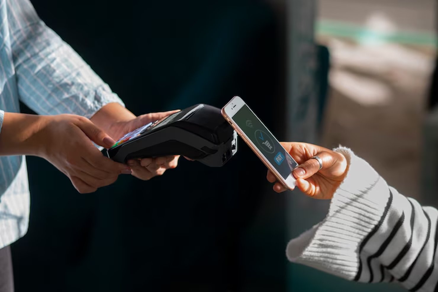 Una persona effettua un pagamento contactless con uno smartphone utilizzando carte di credito digitali, avvicinando il dispositivo a un terminale POS tenuto da un'altra persona. L'immagine rappresenta un ambiente moderno e tecnologico per i pagamenti.