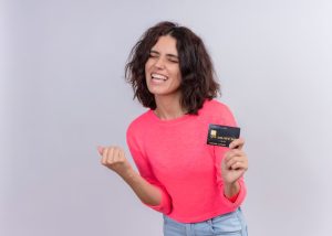 Giovane donna con capelli ricci e maglia rosa sorride entusiasta mentre mostra una carta di credito nera, esprimendo soddisfazione e libertà finanziaria. L’immagine è ideale per rappresentare offerte di carte di credito senza canone annuo in Italia, pensate per chi cerca vantaggi senza costi nascosti.