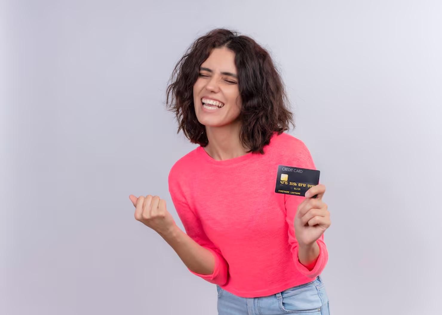 Giovane donna con capelli ricci e maglia rosa sorride entusiasta mentre mostra una carta di credito nera, esprimendo soddisfazione e libertà finanziaria. L’immagine è ideale per rappresentare offerte di carte di credito senza canone annuo in Italia, pensate per chi cerca vantaggi senza costi nascosti.