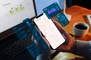Uomo che utilizza uno smartphone e un laptop con interfacce grafiche fluttuanti di dati e statistiche, simbolo dell’interconnessione e dell’analisi nell’economia digitale.