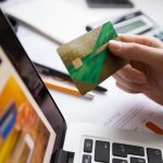 Persona che tiene in mano una delle carte di credito attente alla sostenibilità davanti a un computer portatile, simbolo di acquisti online consapevoli e gestione finanziaria eco-responsabile.