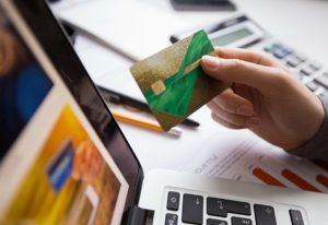 Persona che tiene in mano una delle carte di credito attente alla sostenibilità davanti a un computer portatile, simbolo di acquisti online consapevoli e gestione finanziaria eco-responsabile.