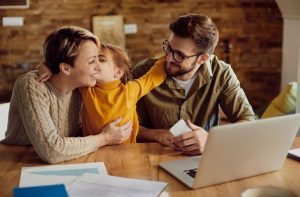 Famiglia seduta al tavolo con documenti e computer portatile, che sorride mentre discute insieme, rappresentando un momento di pianificazione finanziaria familiare in un ambiente domestico sereno.