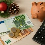La foto mostra una composizione ordinata con banconote e monete in euro, un salvadanaio in terracotta, un ramoscello di pino decorato con una palla natalizia e una calcolatrice su un tavolo chiaro. L’immagine richiama il tema della gestione finanziaria e della pianificazione della tredicesima durante il periodo natalizio in Italia.