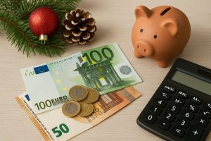 La foto mostra una composizione ordinata con banconote e monete in euro, un salvadanaio in terracotta, un ramoscello di pino decorato con una palla natalizia e una calcolatrice su un tavolo chiaro. L’immagine richiama il tema della gestione finanziaria e della pianificazione della tredicesima durante il periodo natalizio in Italia.